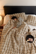 Person lying on a bed covered with a fluffy beige blanket, with a nightstand and lamp in the background.