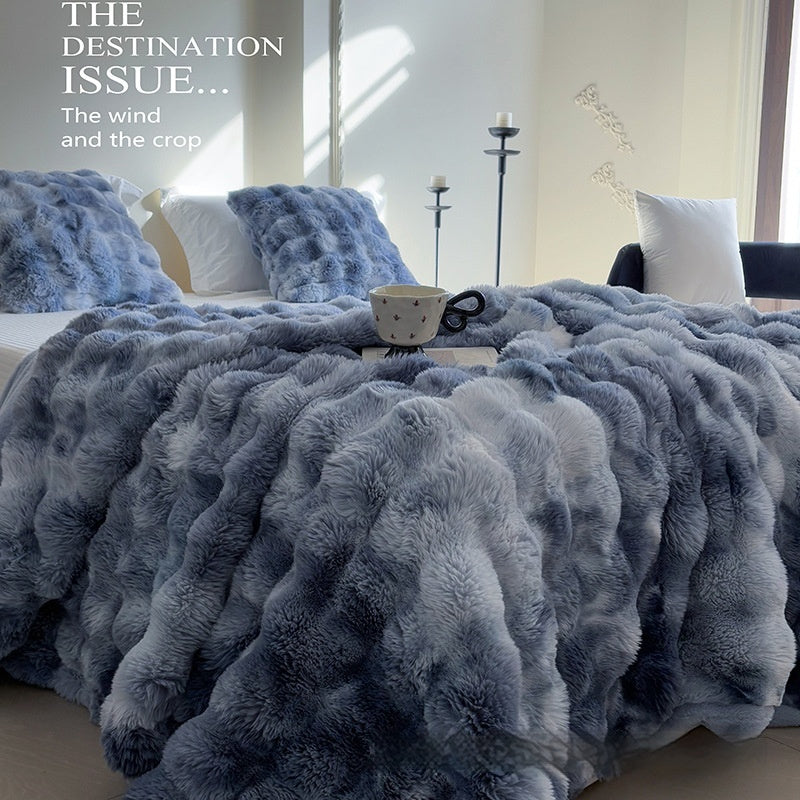 Fluffy gray blanket on a bed with pillows and a cup in a bedroom setting.