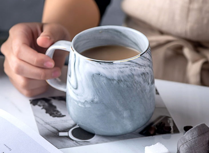 Person holding a marble-patterned mug with a drink on a newspaper