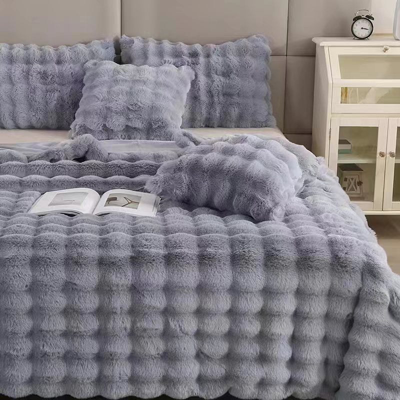 Gray textured blanket and pillows on a bed in a bedroom setting.